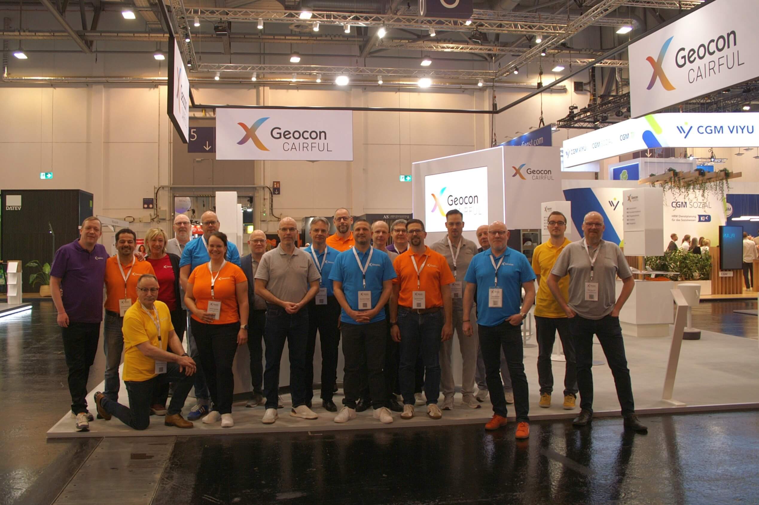Eine Gruppe von Fachleuten steht lächelnd vor dem Geocon-Stand auf einer Messe, gekleidet in farbenfrohe T-Shirts.